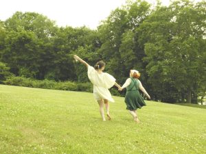 Two girls prancing through a meadow.